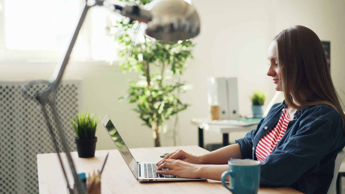 A person working remotely on a laptop from a bright home office